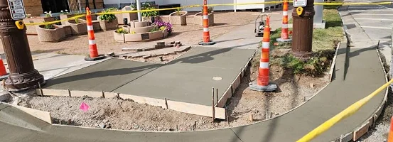 A construction site featuring several orange cones placed around the area, with a view of the ground and surrounding outdoor elements.