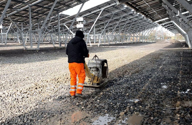 An employee using a vibrating machine compresses the rubble on the future Parking lot