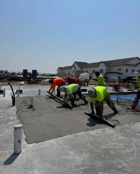 Construction workers pouring concrete on a slab, wearing safety gear and focused on their task