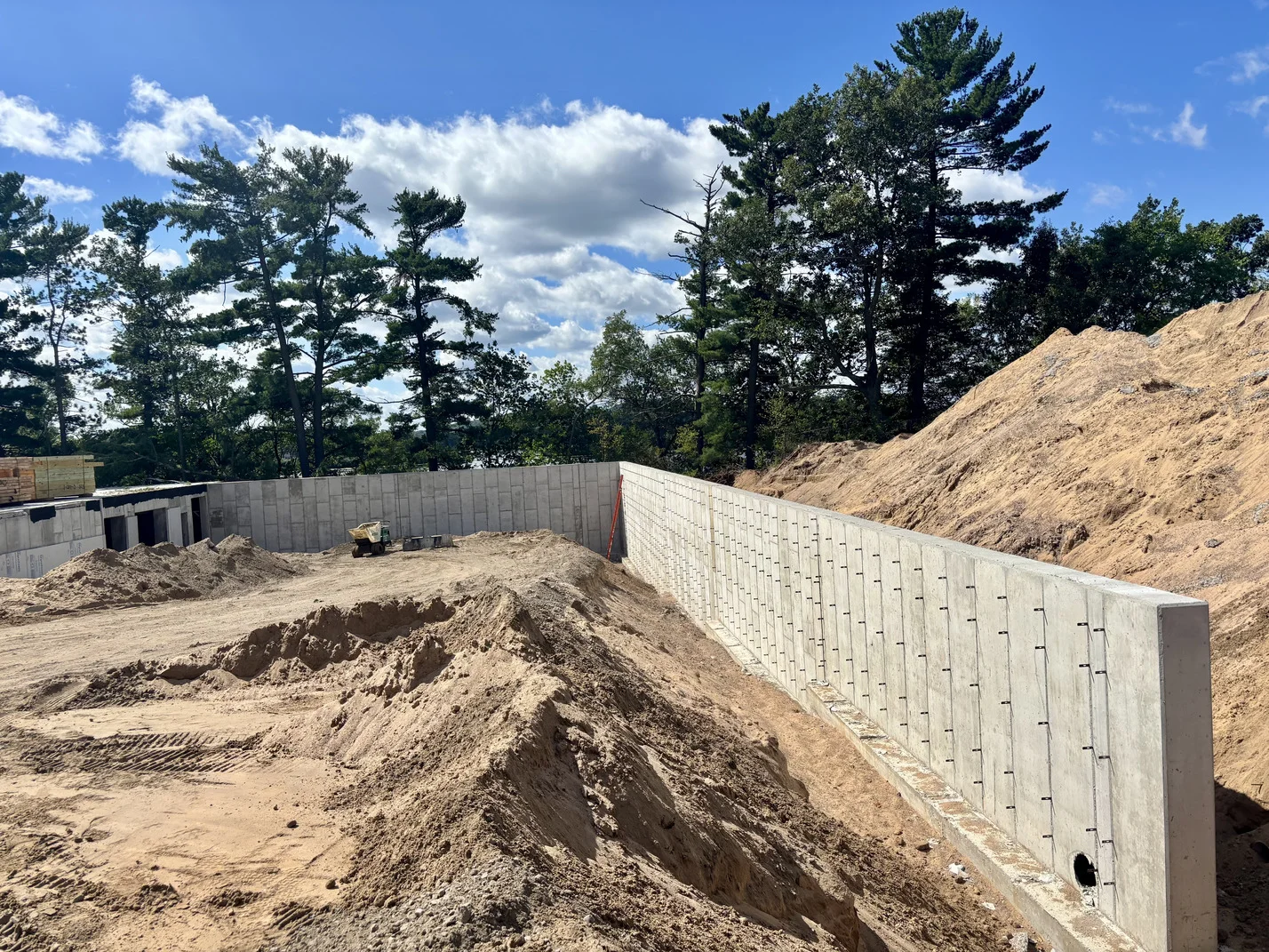 A construction worker builds a concrete wall in a dirt field, surrounded by earth and construction materials