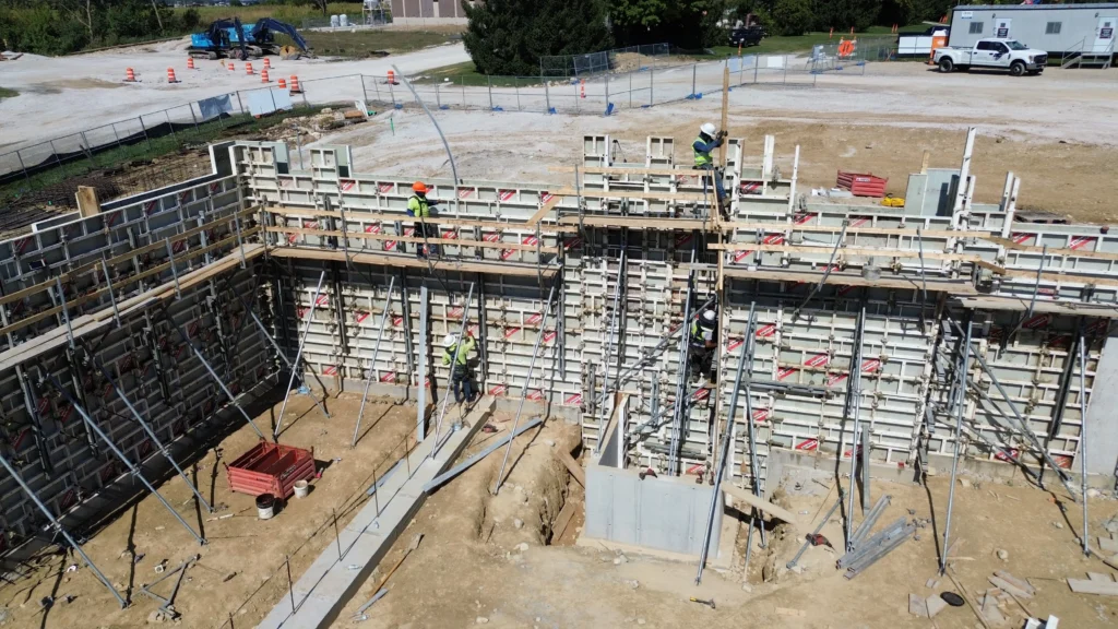 Construction site with workers assembling concrete formwork walls wearing safety gear.