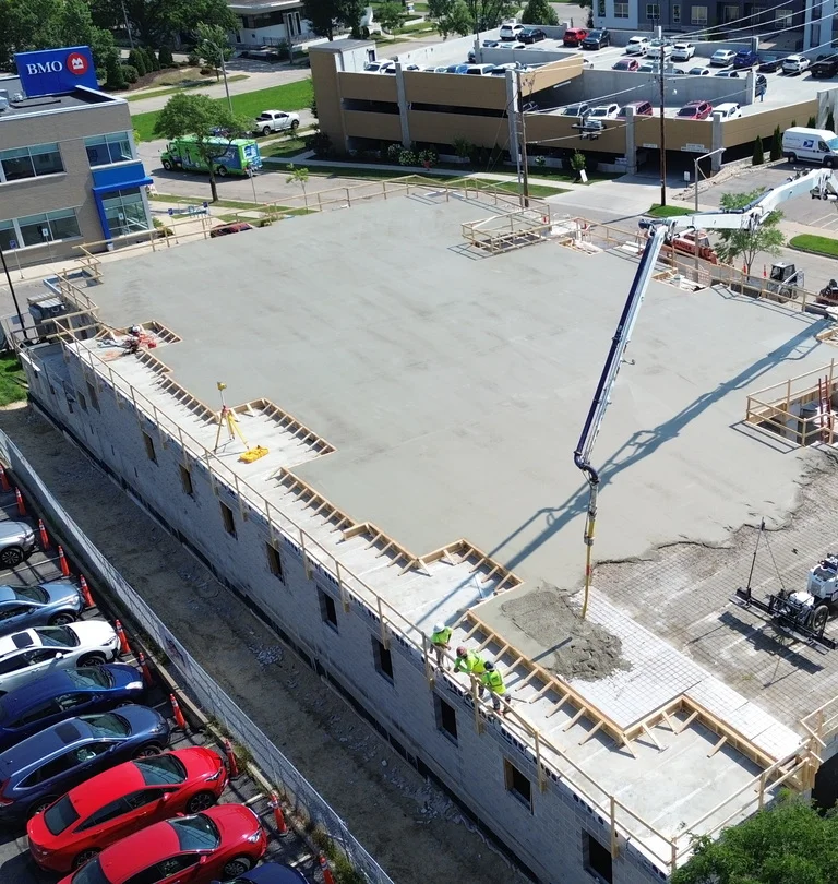 Aerial view of a construction site with workers pouring concrete on a building's roof.