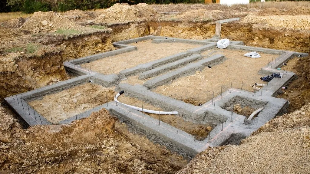 Excavated construction site with concrete foundation footings and embedded pipes.