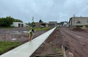 Construction worker smoothing newly poured concrete sidewalk on overcast day in urban area.