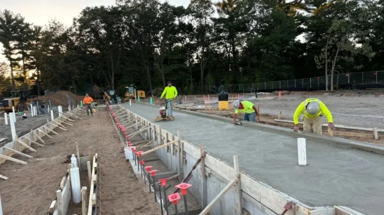 Construction workers in bright safety attire smoothing freshly poured concrete on an outdoor site.