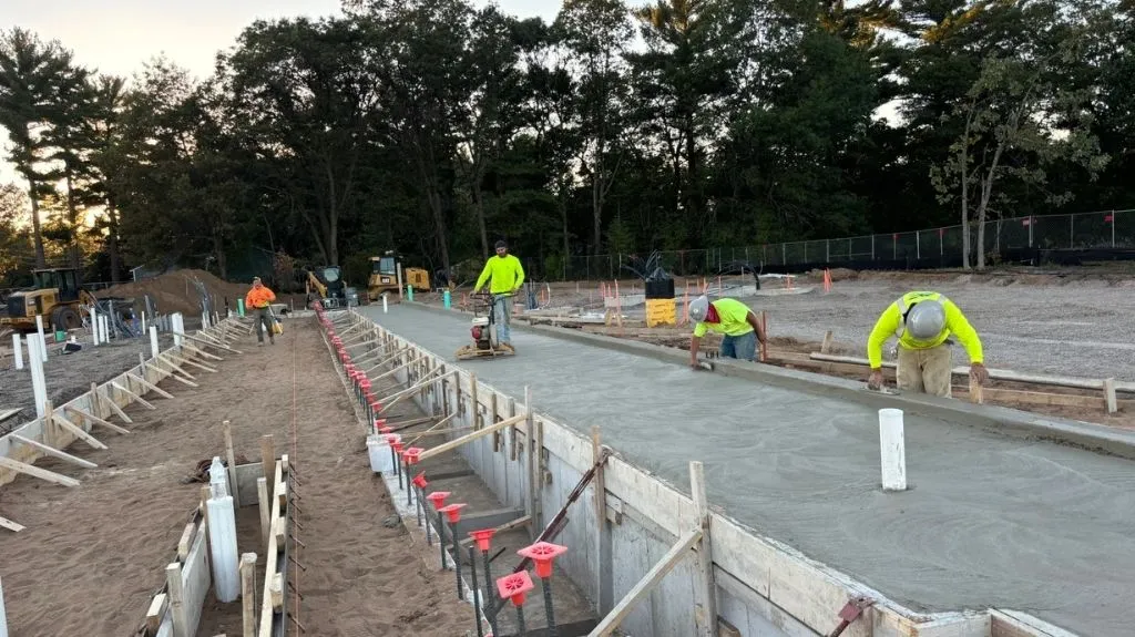 Construction workers in bright safety attire smoothing freshly poured concrete on an outdoor site.