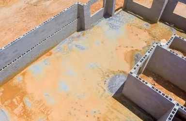 Aerial view of a construction site with partially built concrete block walls on sandy ground.
