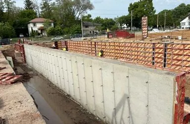 Construction site featuring a large concrete retaining wall with workers and wooden framework.