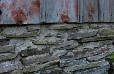 Close-up of a weathered stone wall with a wooden panel above it.
