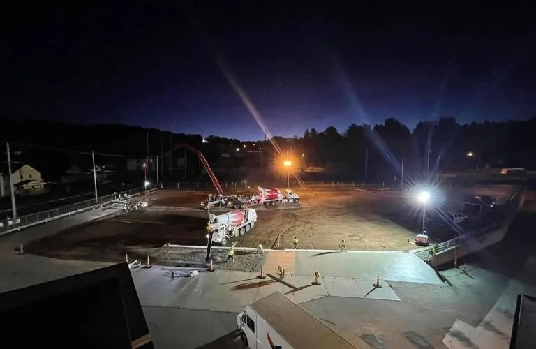 Nighttime construction site with cement mixer trucks, workers, and bright floodlights.