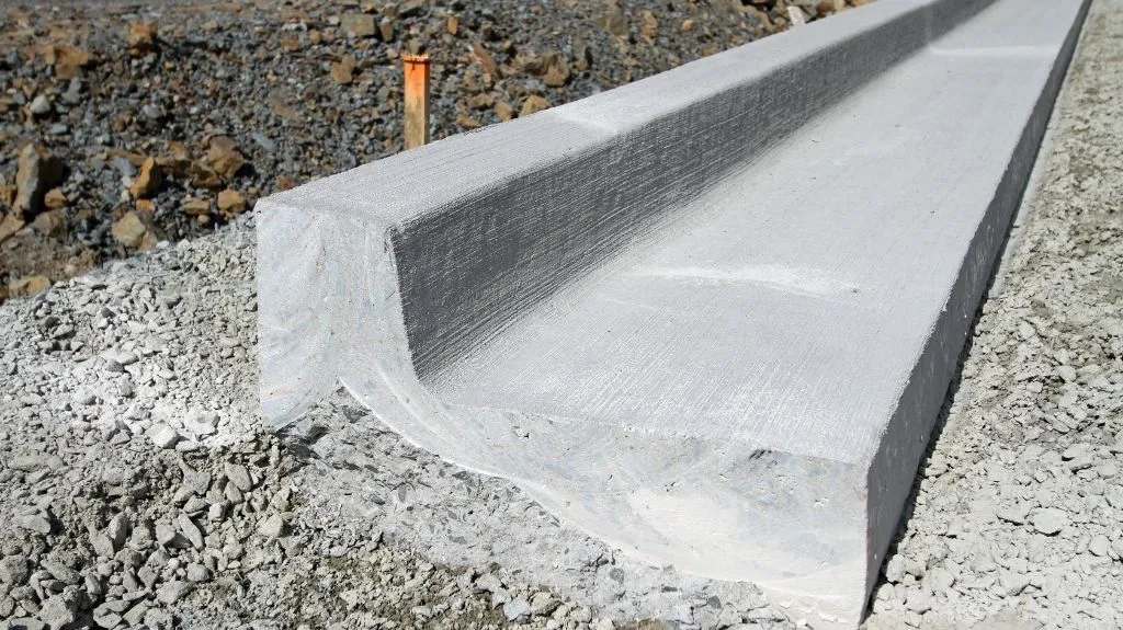 Close-up of a newly installed concrete drainage channel on a gravel surface.
