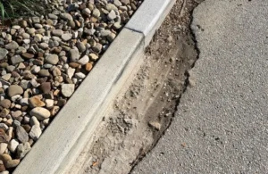 Close-up of a concrete curb adjacent to a gravel bed and damaged asphalt pavement.