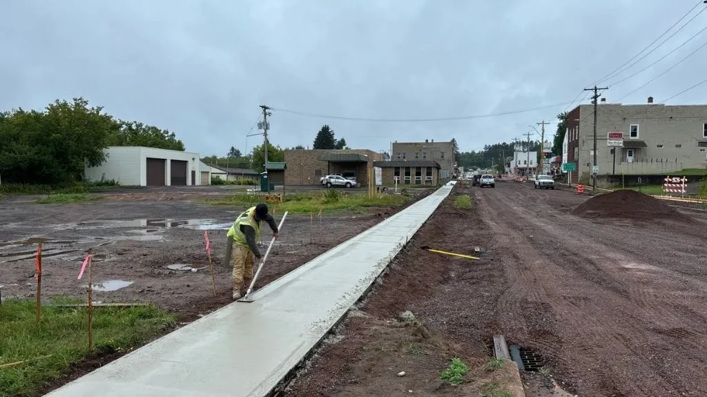 Construction worker smoothing wet concrete on a newly paved sidewalk in a small town.